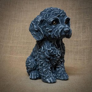 May include: A detailed, dark gray dog figurine with a curly coat and brown eyes. The dog is in a seated position, with its paws neatly placed. The sculpture has a textured appearance, adding depth and realism to the design. The figurine is a decorative item.