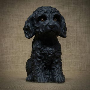 May include: A black dog statue with curly fur and brown eyes. The dog is sitting upright, with its front paws together. The statue has a matte finish and is set against a neutral background.