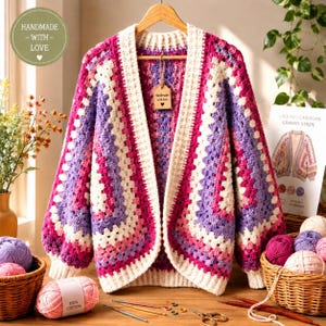 Peut inclure: Un cardigan au crochet avec un motif à rayures granny dans des tons rose, violet et blanc. Le vêtement présente des manches longues, une bordure blanche côtelée le long de l'ouverture avant et une étiquette Handmade with love au col.
