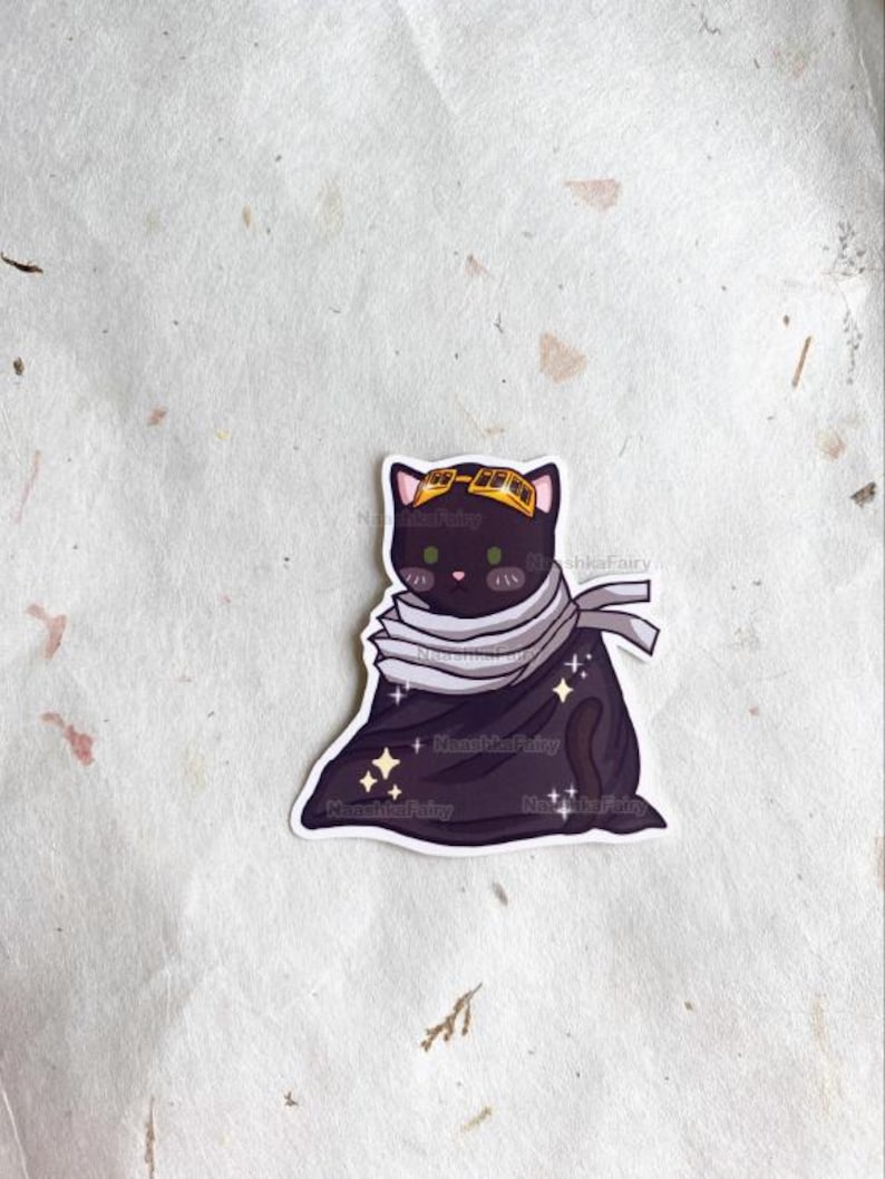 May include: A sticker of a black cat with green eyes, wearing a yellow headband and a grey scarf. The cat is also wearing a dark purple cloak with sparkles. The sticker has the text "NooshkaFairy".