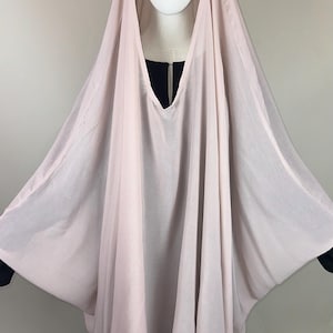 Könnte beinhalten: Ein hellrosa Hijab mit V-Ausschnitt, drapiert über einem Schaufensterpuppenkopf. Eine lila Rose ist an der Kopfbedeckung befestigt. Der Hijab wird über einem schwarzen Kleidungsstück getragen.