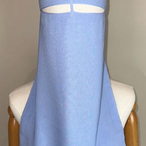 May include: A light blue niqab, a traditional Islamic veil, displayed on a mannequin. The veil features a head covering and a face veil with eye slits. The fabric appears to be a lightweight, textured material.
