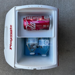 May include: A white and red Playmate cooler with a red Coca-Cola can and two water bottles inside. The Coca-Cola can has the words "RECYCLE ME" printed on it. The cooler is open, revealing the contents.