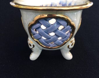 Puede incluir: Un pequeño cuenco de cerámica blanca con patas, con borde y detalles dorados. El cuenco presenta un diseño azul tejido en el lateral y está decorado con motivos florales dorados. El interior tiene detalles florales azules.