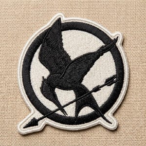 May include: Embroidered patch featuring a black bird with outstretched wings and an arrow, set against a white circle with a black border. The patch has a white border and is likely for clothing or accessories.