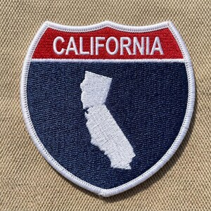 May include: A shield-shaped patch featuring the word "CALIFORNIA" in white letters on a red background. Below, a blue field displays a white outline of the state. The patch has a white stitched border.