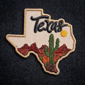 May include: Embroidered patch in the shape of Texas, featuring a desert landscape with a cactus, mountains, and a sun. The word "Texas" is stitched in black script. The patch has a tan border and is set against a dark blue background.