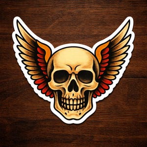 May include: A sticker featuring a detailed illustration of a skull with large, stylized wings. The skull is a light tan color with black eye sockets and teeth. The wings are tan, orange, and red, with a black outline. The sticker has a white border.
