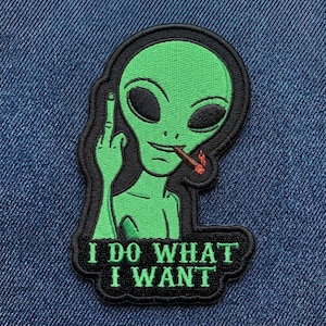 May include: Embroidered patch featuring a green alien with black eyes, smoking a cigarette, and giving the middle finger. The patch has the text "I DO WHAT I WANT" in white letters on a black background.