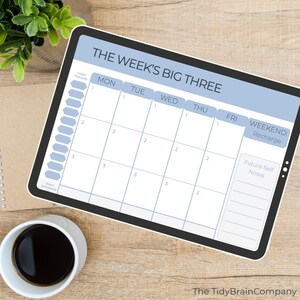 Pode incluir: Um planejador semanal digital com o texto "THE WEEK'S BIG THREE" em azul e branco. O planejador inclui seções para cada dia da semana, um rastreador de hábitos e espaço para anotações. Uma xícara de café e uma planta estão no fundo.