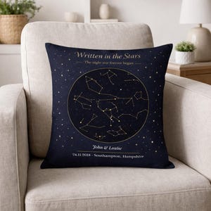 May include: A navy cushion with a gold constellation design. The text "Written in the Stars" is above a circular constellation map. The names "John & Louise" and a date and location are below.