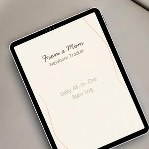 Pode incluir: Um tablet digital exibindo um diário de bebê. A tela mostra o texto "From a Mom Newborn Tracker" e "Daily All-in-One Baby Log" em uma fonte suave e elegante. O tablet tem uma moldura preta e uma tela de cor clara.
