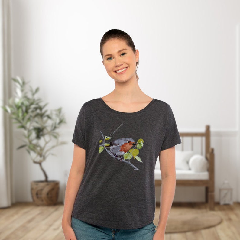Puede incluir: Una camiseta gris oscuro con una ilustraci&oacute;n de acuarela de un petirrojo posado en una rama con hojas verdes.