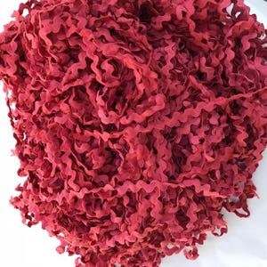 May include: A close-up of a pile of red, wavy trim. The trim is made of a soft, fabric-like material.