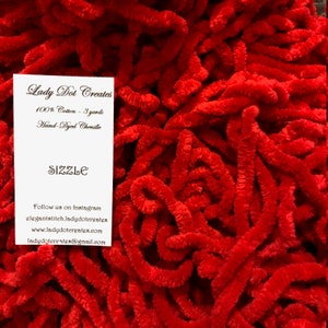 May include: A close-up of a pile of red chenille stems, also known as pipe cleaners. The stems are 3 yards long and made of 100% cotton. The label reads "Lady Dot Creates" and "Sizzle".