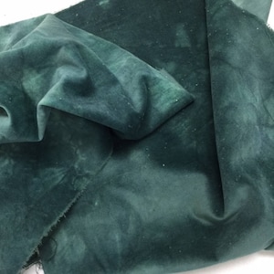 May include: A piece of dark green velvet fabric with a mottled, tie-dye pattern. The fabric is folded and draped, showing its texture and drape.