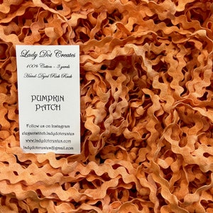May include: A close-up of a pile of orange hand-dyed rick rack trim. The trim is 100% cotton and is 3 yards long. The label reads "Lady Dot Creates Pumpkin Patch".