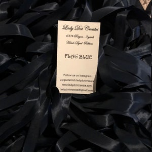 May include: A close-up of a pile of dark blue rayon ribbon. The ribbon is hand-dyed and measures 3 yards in length. The card reads "Lady Dot Creates 100% Rayon - 3 yards Hand Dyed Ribbon FLAG BLUE Follow us on Instagram elegantstitch.ladydotergates www.ladydotergates.com ladydotergates@gmail.com"