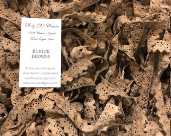 May include: A close-up image of a pile of brown cotton lace trim. The lace is hand-dyed and is 100% cotton. The image includes a business card with the text "Lady Dot Creates", "100% Cotton - 2 yards", "Hand-Dyed Love", "Buster Browns", "Follow us on Instagram", "elegantstitch.ladydotcreates", "www.ladydotcreates.com", and "ladydotcreates@gmail.com".