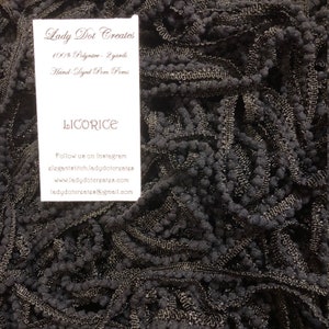 May include: Close-up of black hand-dyed pom poms. The tag reads "Lady Dot Creates" and "LICORICE". The pom poms are made of 100% polyester and are 2 yards in length. Contact information is also included on the tag.
