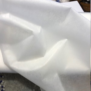 May include: White non-woven fabric, a type of synthetic material often used for crafts, masks, and other projects.