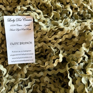 May include: A close-up of a pile of olive green rick rack trim. The trim is 100% cotton and is 3 yards long. The card reads "Lady Dot Creates" and "Olive Branch".