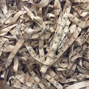 May include: A pile of vintage fabric measuring tapes in a beige color with black markings. The tapes are tangled and overlapping.