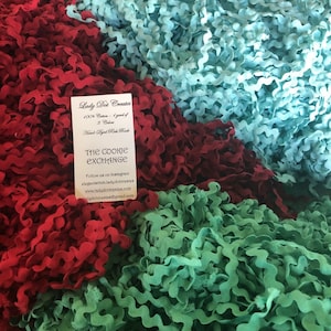 May include: A close-up of three spools of wavy trim in red, green, and blue. The spools are labeled "Lady Dot Creates" and "The Cookie Exchange".