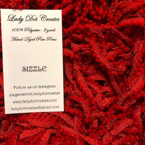 May include: A close-up of a pile of red pom-pom trim. The trim is made of 100% polyester and is 2 yards long. The trim is hand-dyed and is labeled "Sizzle". The label also includes the text "Lady Dot Creates" and contact information for the seller.