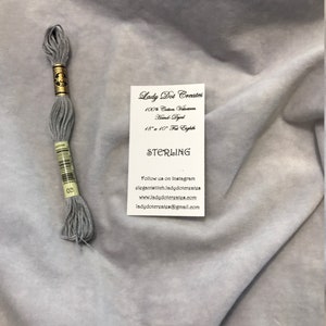 May include: A skein of light gray embroidery floss with a label that reads "Lady Dot Creates 100% Cotton Vdoctoon Hand-Dyed 18" x 10" Fat Eighth STERLING 03 Follow us on Instagram elegantstitch.ladydotergates www.ladydotergates.com ladydotergates@gmail.com"