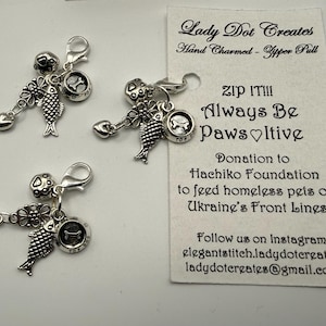 May include: Three silver-toned zipper pulls with various charms, including a fish, a heart, and a dog bone. The charms are attached to a lobster clasp. A white card with text that reads "ZIP IT!!! Always Be PawsItive" is in the background.