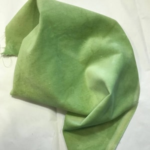 May include: A piece of green fabric with a gradient of color from a lighter green to a darker green. The fabric is folded and has a soft, textured surface.