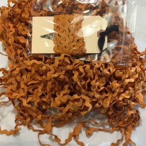 May include: A large pile of orange wavy trim, a type of fabric trim used for sewing and crafting projects. The trim is packaged in a clear plastic bag with a small tag that says "The Ribbon Retreat".