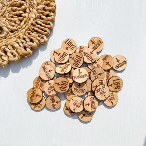 May include: A collection of small, round wooden tokens with engraved words and a cross symbol. Words include "Light," "Truth," "Love," and "Jesus." A woven, circular placemat is in the background.