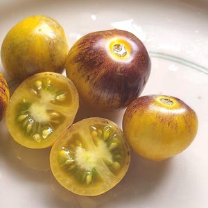 May include: Close-up of several heirloom tomatoes, some whole and some halved. The tomatoes are a mix of yellow and deep purple with green interiors. The halved tomatoes reveal the seeds and juicy flesh.