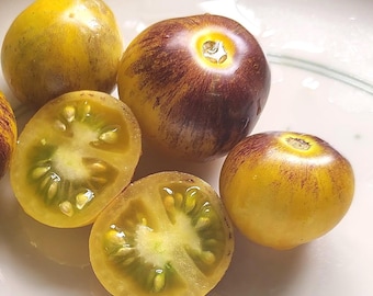 May include: Close-up of several heirloom tomatoes, some whole and some halved. The tomatoes are a mix of yellow and deep purple with green interiors. The halved tomatoes reveal the seeds and juicy flesh.