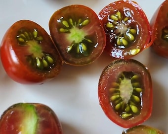May include: Close-up of several halved heirloom tomatoes. The tomatoes have a deep red skin with a dark brown hue. The interior reveals a vibrant green core with yellow seeds, showcasing a juicy texture.