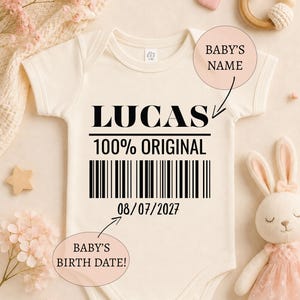 Peut inclure: Un body pour bébé de couleur crème avec le texte noir LUCAS, 100% ORIGINAL et la date 08/07/2027. Le motif comprend un code-barres noir centré sur la poitrine. Le vêtement possède des manches courtes et une encolure ronde.