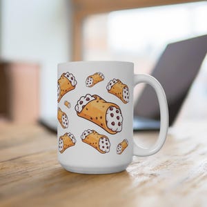 May include: White ceramic coffee mug featuring a repeating pattern of cartoon cannoli pastries. The cannoli are depicted with a golden-brown shell, white cream filling, and chocolate chip accents. The mug has a large handle.