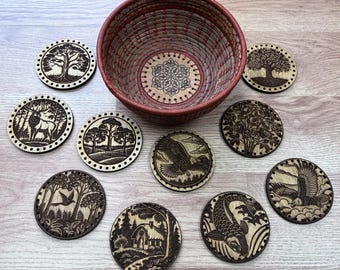 May include: A set of ten wooden coasters with various nature-themed designs, including a deer, a bird, a tree, a fish, and a bird in flight. The coasters are arranged around a red and white woven basket.