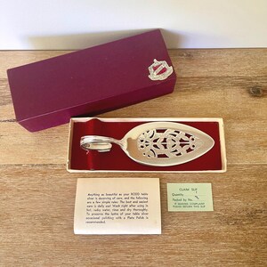 May include: A silver pie server with a floral design, presented in a red-lined box with a burgundy lid. Includes a care instruction card and a claim slip.