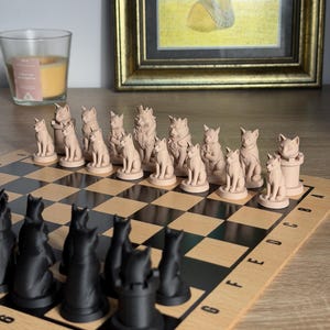 Peut inclure: Un jeu d'échecs sur le thème des chats. Les pièces d'échecs sont sculptées en forme de chats, les pièces blanches étant de couleur beige clair et les pièces noires étant noires. L'échiquier est en bois avec des cases noires et beiges.