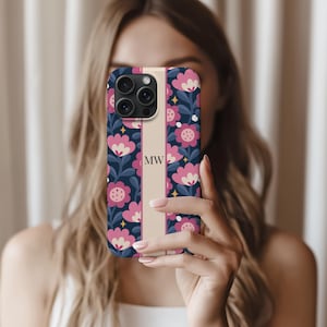 May include: A smartphone case with a floral design. The case features a navy blue background with pink flowers and white leaves. A vertical beige stripe runs down the center with the initials "MW".