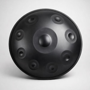 May include: A black steel handpan instrument with a rounded shape and multiple circular indentations. The instrument has a central dome and a smooth, matte finish. The handpan is designed for melodic percussion and is often used in meditative music.
