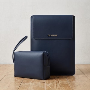 Peut inclure: Une housse pour ordinateur portable rectangulaire bleu marine avec un rabat et le texte doré GLYMMR, accompagnée d'une pochette rectangulaire zippée assortie bleu marine avec une dragonne. Les deux articles ont une finition lisse et unie.