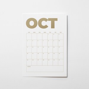 K&ouml;nnte beinhalten: Ein wei&szlig;es Kalenderblatt f&uuml;r den Monat Oktober mit gro&szlig;en beigen Buchstaben, die oben OCT bilden. Das Raster zeigt die Wochentage von Sonntag bis Samstag mit nummerierten Daten von 1 bis 31 und einem Notizbereich am unteren Rand.
