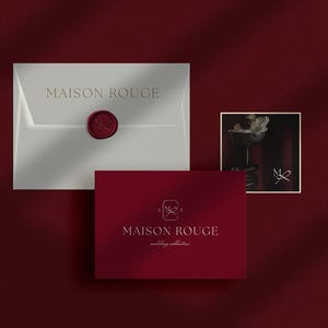 Puede incluir: Presentación de papelería "MAISON ROUGE" sobre fondo rojo oscuro. El conjunto incluye un sobre blanco con un sello de cera rojo, una tarjeta roja y una pequeña imagen enmarcada.