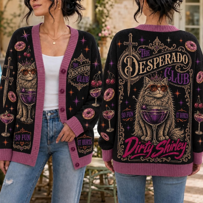 K&ouml;nnte beinhalten: Eine schwarze Strickjacke mit violetten R&auml;ndern und einer Grafik einer Katze mit Sonnenbrille neben einem Cocktailglas. Auf der R&uuml;ckseite steht der Text "The Desperado Club" und "Dirty Shirley" mit Abbildungen von Schwertern, Kirschen und Donuts.