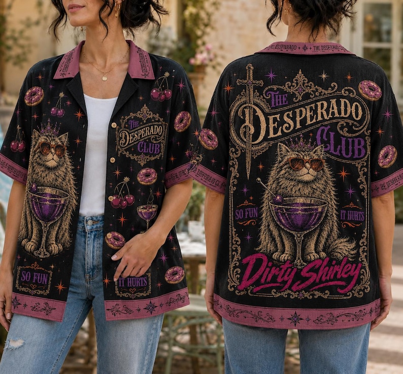 K&ouml;nnte beinhalten: Ein schwarzes kurz&auml;rmeliges Hemd mit Knopfleiste und einer Grafik einer Katze mit Sonnenbrille und Krone, die einen lila Cocktail h&auml;lt. Das Design enth&auml;lt den Text The Desperado Club, So Fun, It Hurts und Dirty Shirley sowie Kirsch- und Donut-Motive.