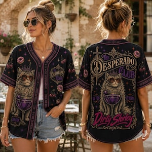 K&ouml;nnte beinhalten: Ein schwarzes Baseballtrikot mit Knopfleiste und einer Grafik einer Katze mit Sonnenbrille, die einen violetten Cocktail h&auml;lt. Das Design enth&auml;lt den Text "The Desperado Club" und "Dirty Shirley" sowie Kirsch- und Donut-Motive.